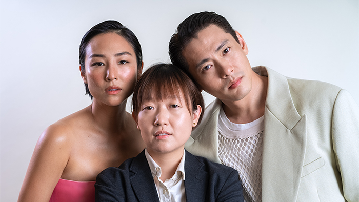 Greta Lee, Celine Song and Teo Yoo pose in front of a white background.